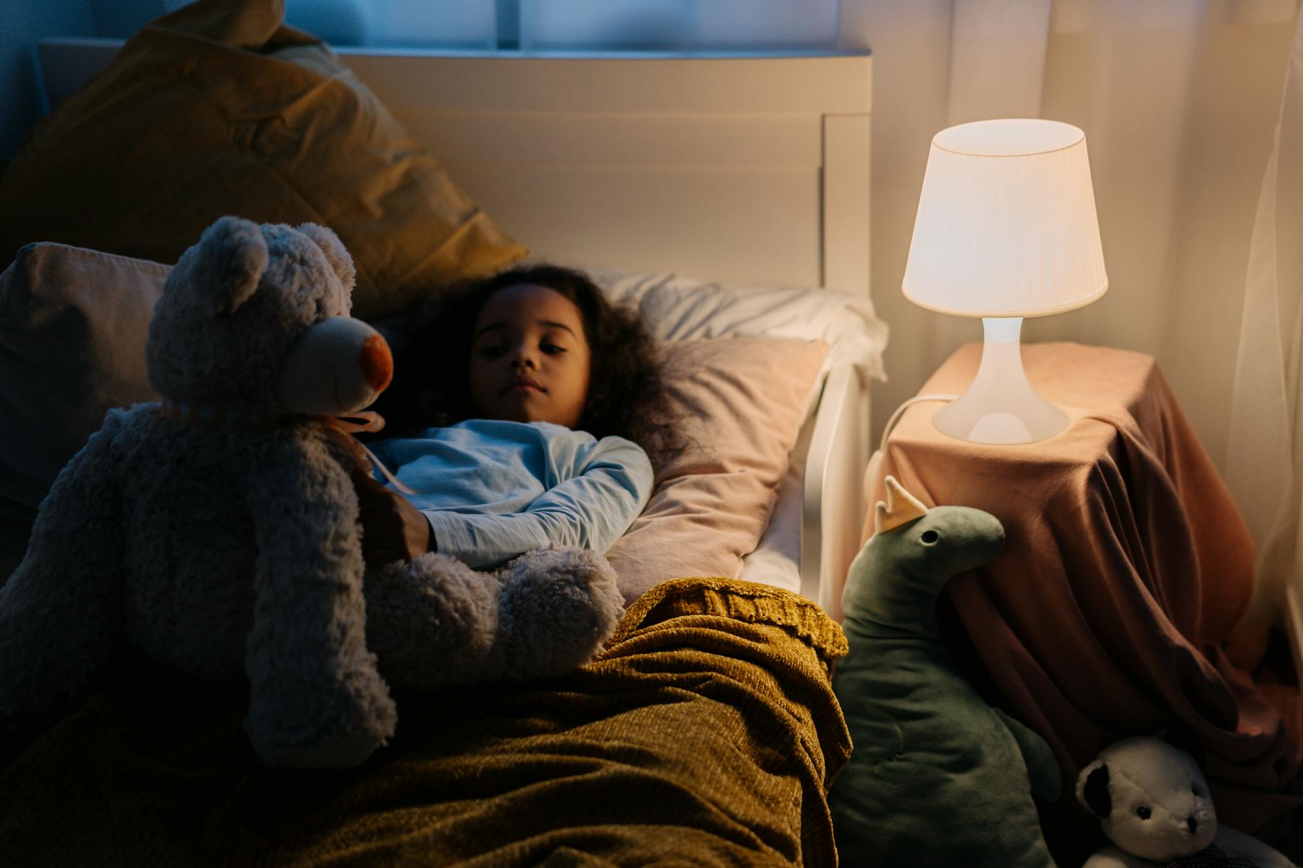 Dziewczynka w łóżku z pluszowym misiem, przy świetle lampki nocnej