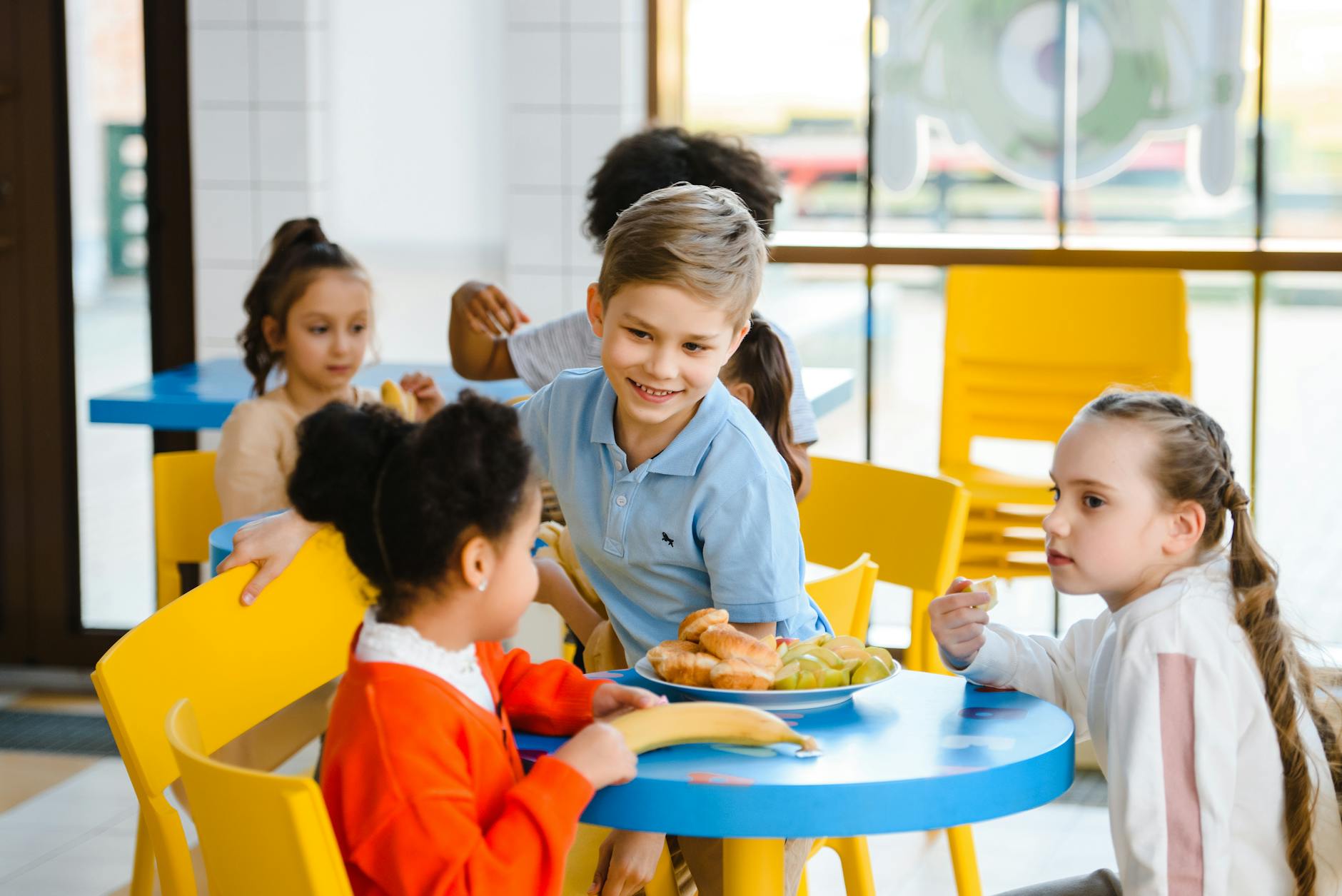 Uśmiechnięte dzieci jedzą wspólny zdrowy lunch w jasnej szkolnej stołówce