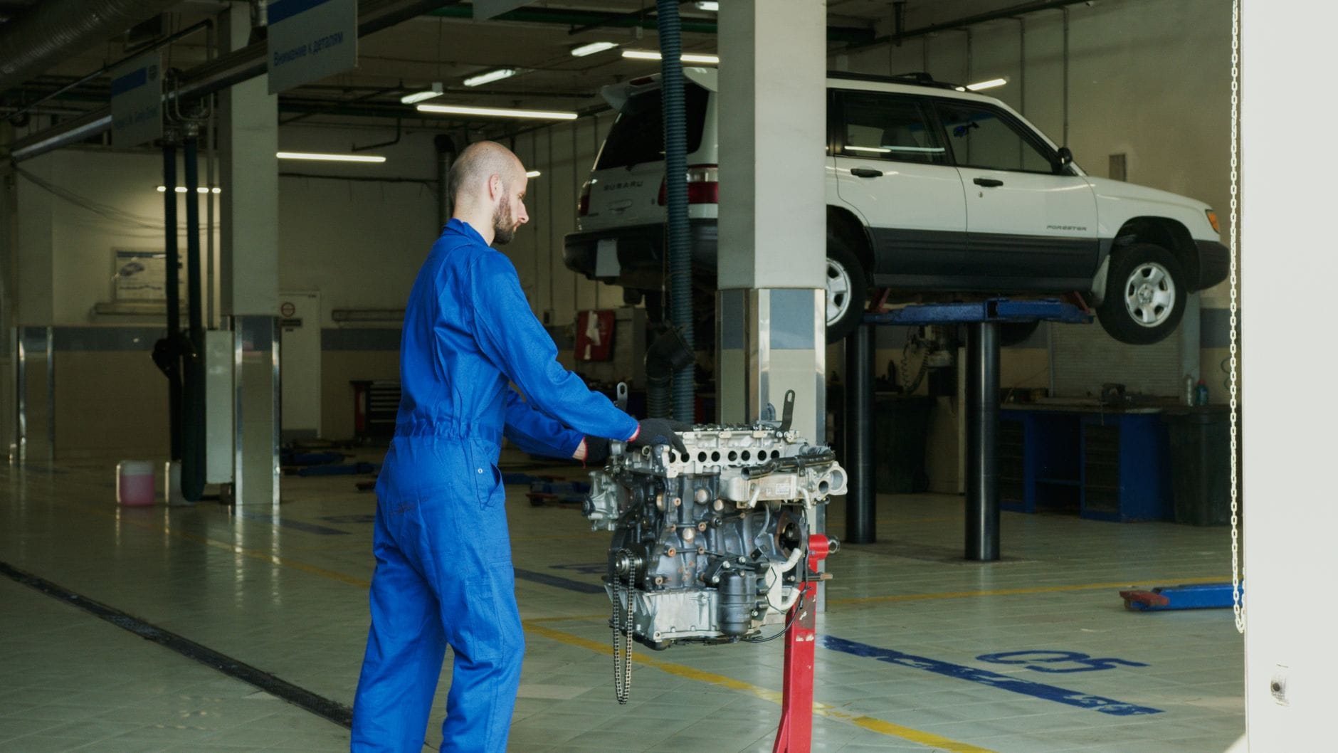 Mechanik w niebieskim kombinezonie naprawia silnik w warsztacie samochodowym Mechanik w niebieskim kombinezonie naprawia silnik w warsztacie samochodowym