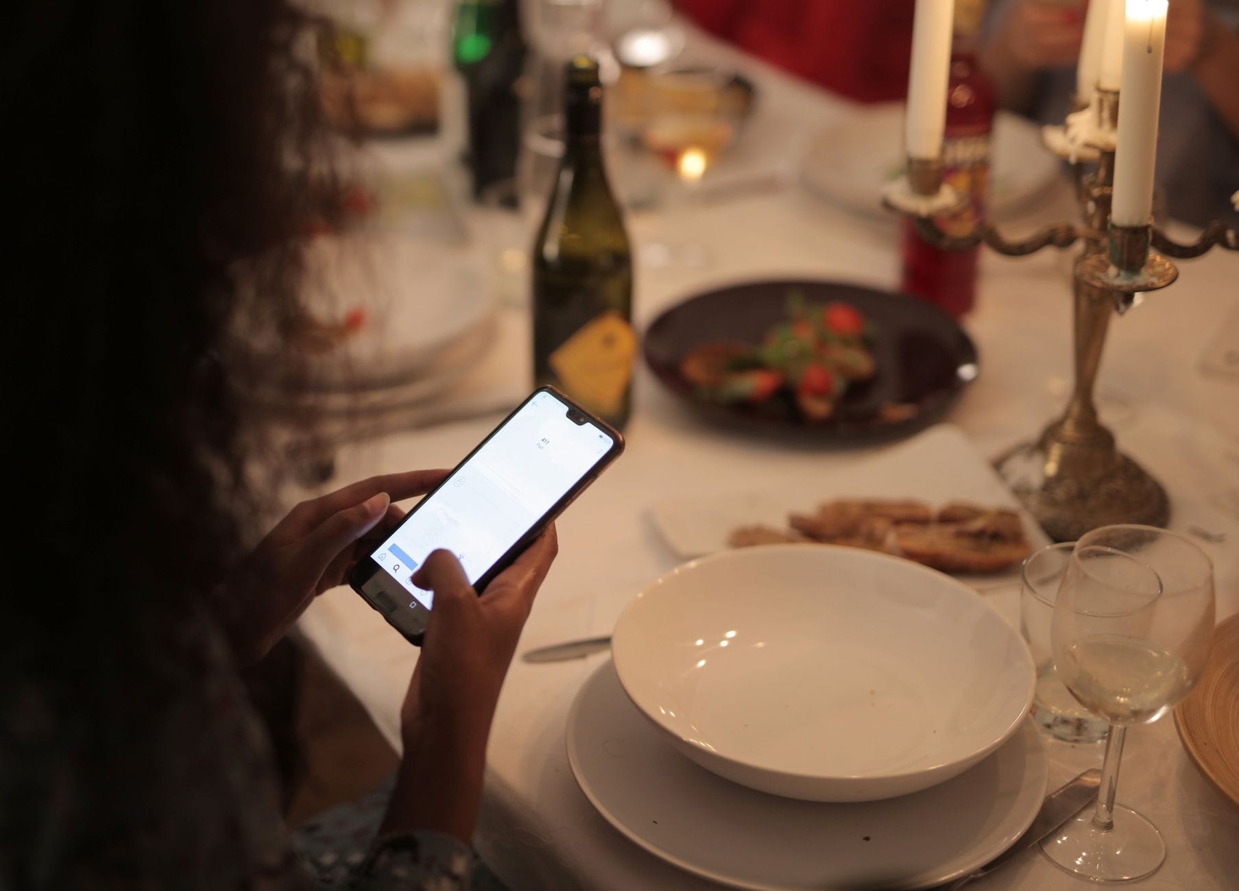 Kobieta przy kolacji przy świecach patrzy w smartfon